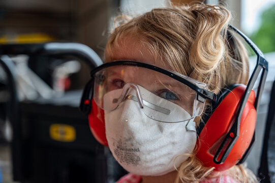 blonde Caucasian little girl wearing a protective dust mask, safety glasses, and hearing protection