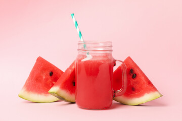 Glass jar of watermelon juice and slices on pink background