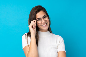 Teenager girl over isolated blue background with glasses and happy