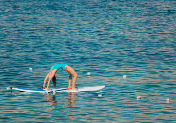 Young woman in blue swimsuite doing yoga on sup board with paddle. Balanced pose - concept of...