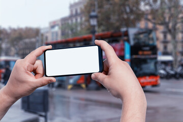 Mockup of the smartphone in the man hands, with a white screen on the background of a tourist bus on a city street. Tourism and travel online.