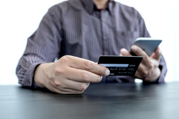 The businessman's hand is holding a credit card and using a smartphone for online shopping and internet payment in the office