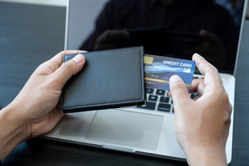 The businessman's hand is holding a credit card and using a laptop for online shopping and internet payment in the office