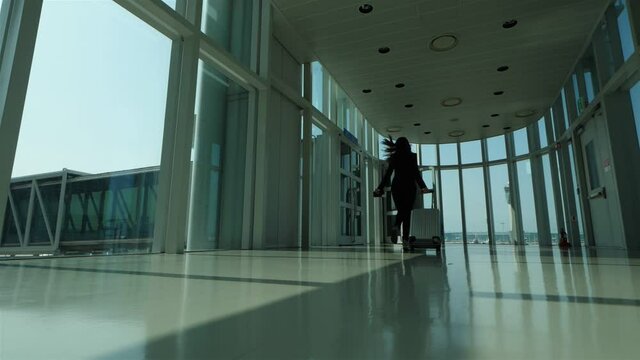 Woman run to boarding bridge with small suitcase, slow motion shot. Passenger hurry and dont want to miss her flight, final call announced, boarding finish. Empty gate passage at modern airport