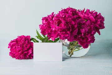 Beautiful burgundy pink peonies stand in a round vase on the table a greeting card. Template for text. Horizontal frame