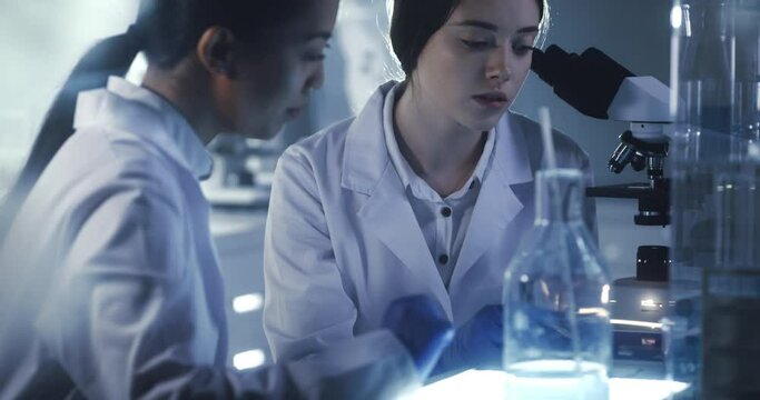 Young female scientists working after hours. Using microscope in futuristic laboratory