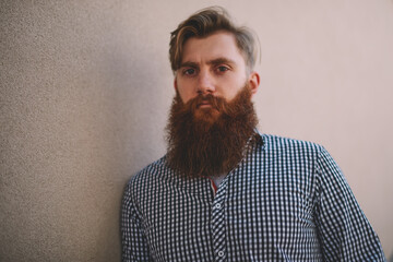 Half length portrait of serious bearded young man dressed in casual stylish shirt looking at camera.Handsome student standing outdoors on promotional background for advertising text message