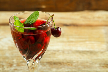 Crystal glass with cherry juice and fresh berries and mint inside on a wooden table.