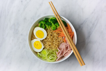 Ramen noodles soup in white bowl with eggs, scallion, chives, broccoli, carrot, top off view, copy space