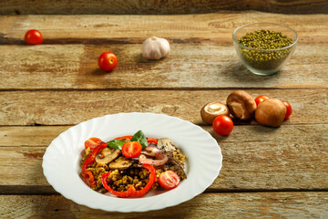 On a wooden table is a white plate of boiled mung bean with mushrooms and vegetables next to the ingredients.