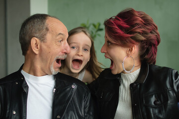 Family portrait of adult daughter with little girl and senior father in loft room with houseplants. Screaming man and woman are in black leather jackets in punk style looking to each other face