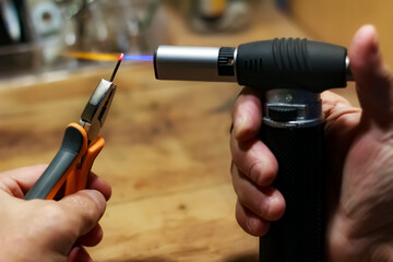 a man heating up a nail, using a torch gun in his workshop