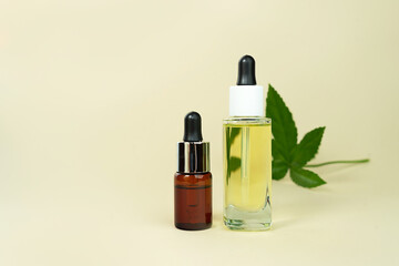 Obraz na płótnie Canvas Glass bottles with herbal CBD oil, THC tincture and hemp leaf on pastel beige background.
