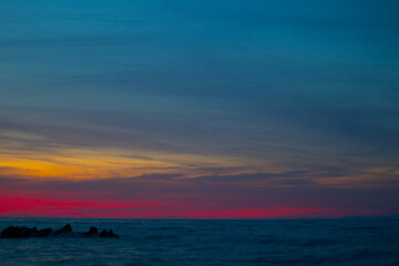 colorful yellow pink sunset on rocky beach with cloudy sky