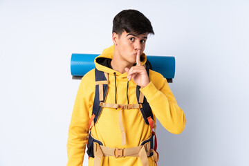Young mountaineer man with a big backpack over isolated blue background doing silence gesture