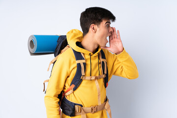 Young mountaineer man with a big backpack over isolated blue background shouting with mouth wide open