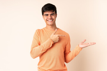 Handsome man over isolated beige background holding copyspace imaginary on the palm to insert an ad