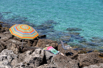 Beach umbrella planted on the rocks and towel on the coast of Otranto, Salento, Puglia, Italy