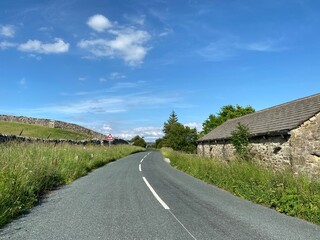 Rural road with long grasses, wild plants and dry stone walls, and an old building near, Grassington, Skipton, UK 
