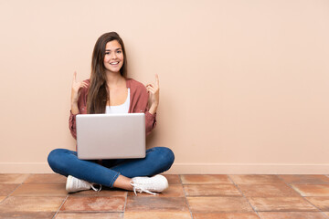Teenager student girl sitting on the floor with a laptop pointing up a great idea - obrazy, fototapety, plakaty