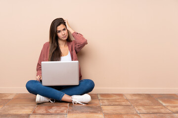 Teenager student girl sitting on the floor with a laptop with an expression of frustration and not understanding