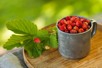 Forest strawberries in a metal Cup on a wooden tray. Concept of berries, summer. Greeting card with berries