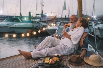 Senior couple drinking champagne and eating tropical fruits on sailboat vacation - Mature people having fun celebrate wedding anniversary on boat trip - Love relationship and travel lifestyle concept