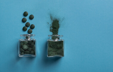 Spirulina algae powder and Chlorella tablets in glass jars on a blue background. Horizontal...