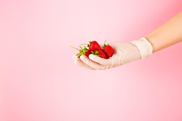 Ripe strawberry with a green stalk in a hand in a glove. Pandemic virus protection concept. Copy space.