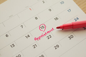Red color marker pen pointing at important appointment schedule on white calendar page date close up