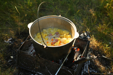 Potato stew in a cauldron with a hanger on an open fire outdoors. Picnics / camping concept
