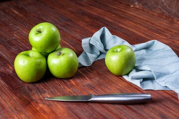 High angle shot of some green apples and a knife and a tablecloth on a wooden surface