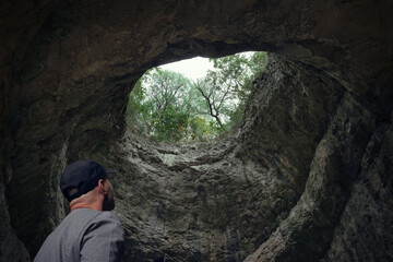Man stands in underground cave looking up at hole in ceiling pouring in sunlight