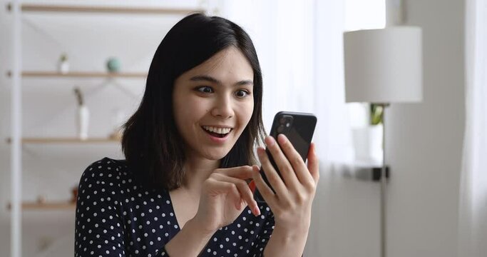 Vietnamese woman holding smart phone look at screen receive read sms clenched fists makes yes I did it gesture feels happy. Career achievement, lottery win, betting auction monetary victory concept