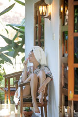 Young woman in silk robe and hair wrapped in a towel enjoy a vacation day in a wooden summer...
