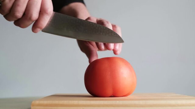 Young man cutting a ripe red tomato into four segments on a wooden board