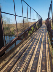 Rusty metal suspended pedestrian bridge over small river Sura in ukraine