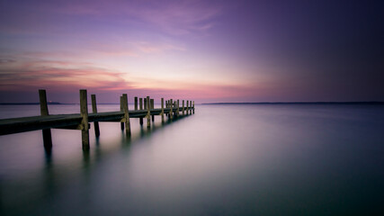 Purple and pink sunset over smooth water and pier