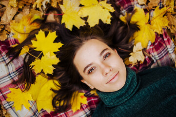 Naklejka na ściany i meble Beautiful girl lies in the yellow autumn leaves. autumn photography. girl and lots of orange leaves