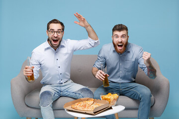 Excited guys friends colleagues in casual shirt sit on couch isolated on blue background. Sport...