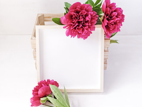 Flower composition. Empty wooden photo frame decorated with lush red peonies. Copy space.
