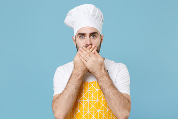 Shocked young bearded male chef or cook baker man in apron white t-shirt toque chefs hat isolated on blue wall background studio. Cooking food concept. Mock up copy space. Covering mouth with hands.