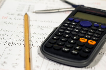 Equations and math writings on notebook with calculator, pencil and compasses