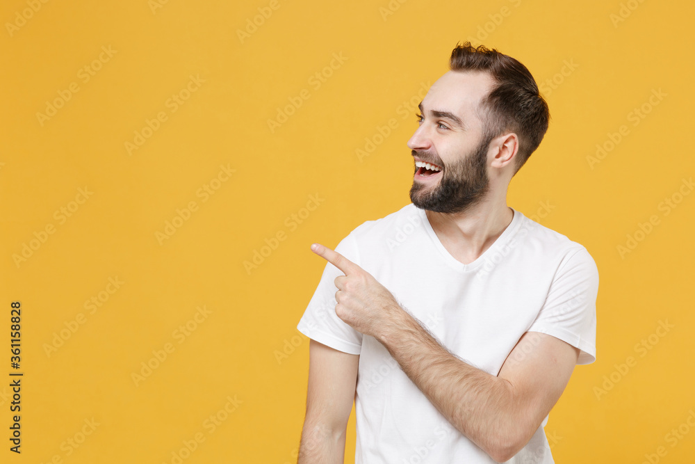 Wall mural cheerful young bearded man guy in white casual t-shirt posing isolated on yellow background studio p