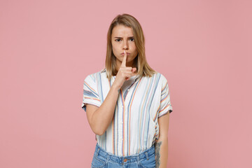Secret young blonde woman girl in casual striped shirt posing isolated on pastel pink background. People lifestyle concept. Mock up copy space. Saying hush be quiet with finger on lips shhh gesture.