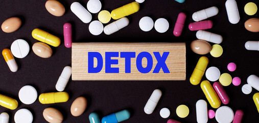 The word DETOX is written on a wooden block among multi-colored tablets on a dark background. Medical concept.