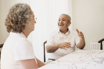 Obraz premium Happy elderly couple, quarantined because of covid-19, sitting together at home, chatting and laughing.