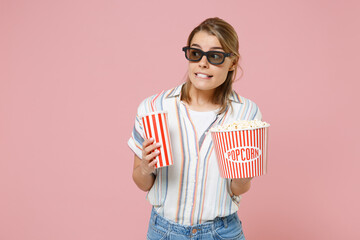 Scared shocked young blonde woman girl in casual striped shirt 3d glasses isolated on pink background. People in cinema, lifestyle concept. Watching movie film, holding bucket of popcorn, cup of soda.