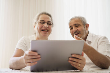 Happy senior couple wave having video call on laptop talking with relatives, smiling aged husband and wife sit on chair at home communicating via online using computer. Elderly and technology concept
