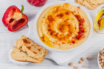 A bowl of chickpeas homemade hummus with olive oil, crispbread and smoked paprika on white wooden background